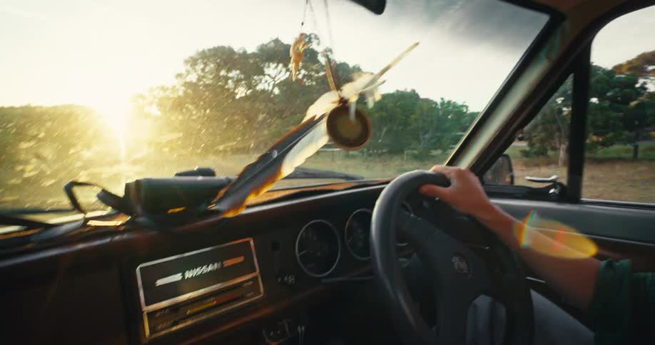 Driver holding the steering wheel while driving along a road with sunlight entering through the windshield