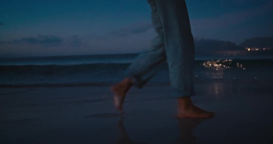 Person walking barefoot on wet beach sand at dusk