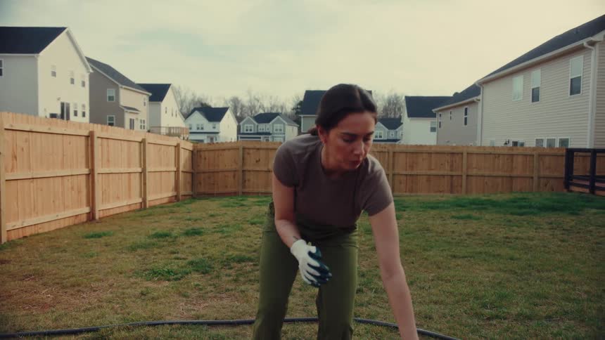 Woman putting on gloves beside a raised garden bed in a residential backyard