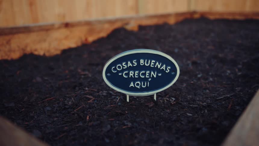 Sign with the text cosas buenas crecen aqu placed in a soil garden bed