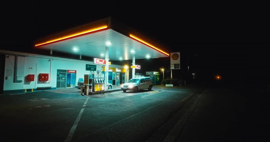 A car driving into a gas station at night with a convenience store beside it surrounded by darkness as the stations lights illuminate the area