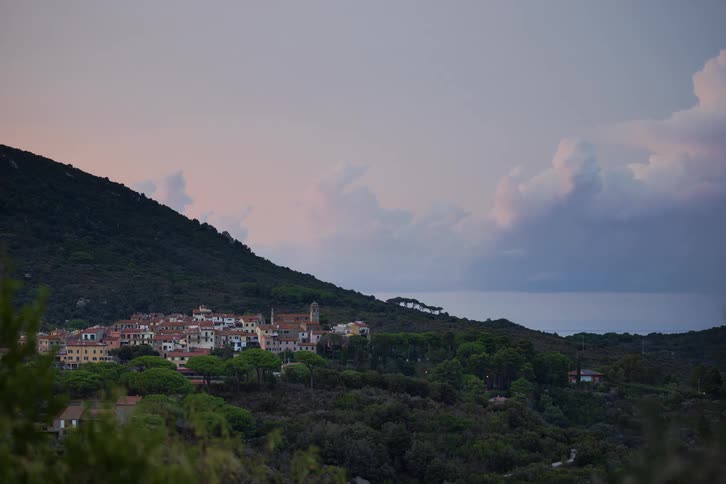 Village at the foot of a forested mountain as clouds move across the sky