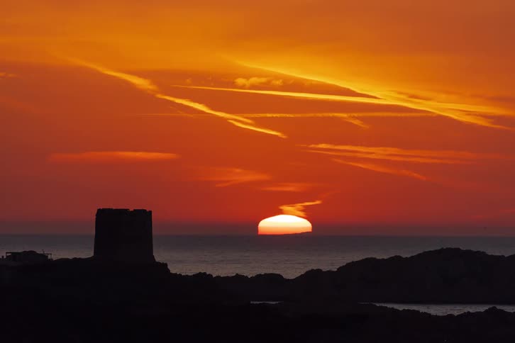 Tower silhouette before the sea under orange sunset sky