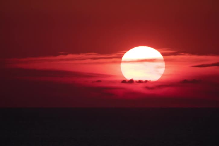 The sun moves behind clouds in an orange sky and sets on the horizon
