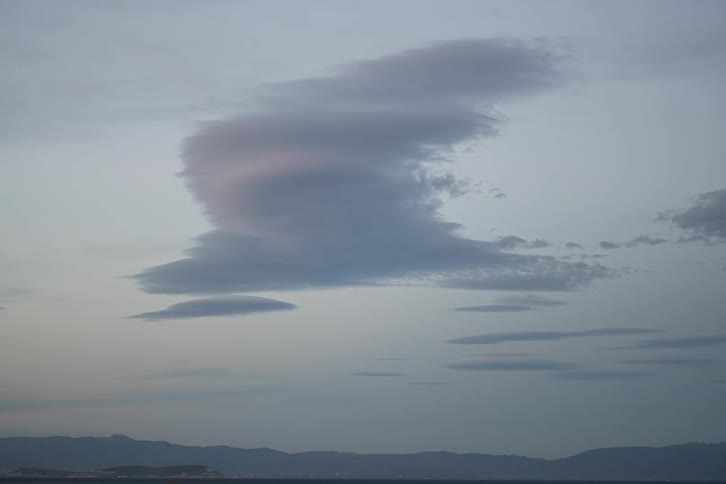 Isolated cloud hovers above mountainous horizon at dusk