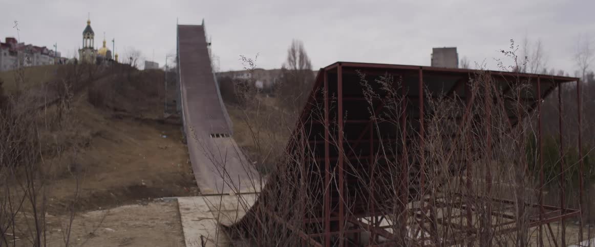 Long ski jump ramp stretches down a hill with metal structure and dry vegetation around