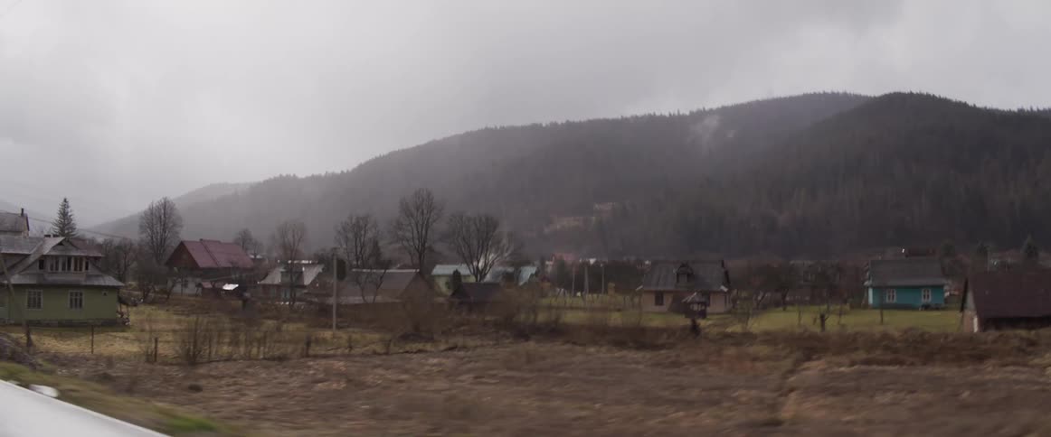Rural house with metal roof in front of forested hills under cloudy sky