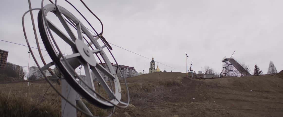 Circular metal structure in foreground before hill with church and jump ramp