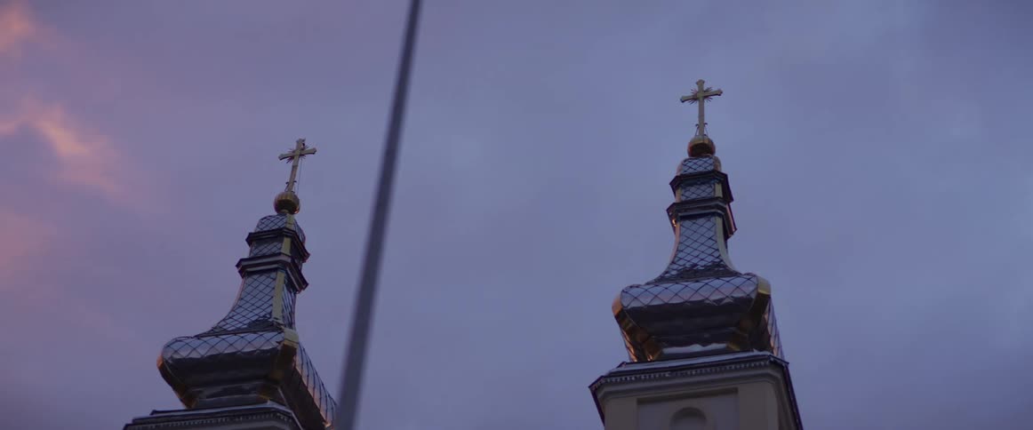 The video features two ornate silverdomed church towers topped with golden crosses against a twilight sky a slow camera movement pans across the structures as the fading sunlight casts a warm pinkish glow on the surrounding clouds