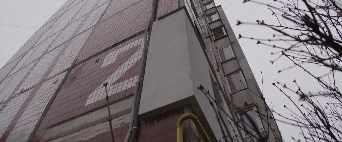 The video shows two prominent lines on the side of a tall apartment buildingthe first is a large lightcolored number 2 integrated into the tiled facade of the building it is composed of square tiles that contrast against the darker reddishbrown til