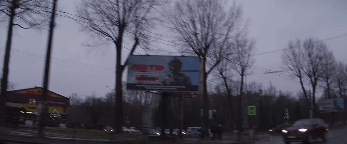 Traffic drives along wet roads passing stores and buildings during a winter evening