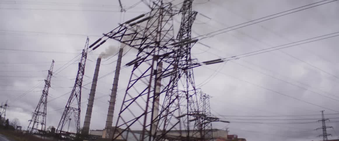 Road parallels power lines passing electric transmission towers and a factory on an overcast winter day
