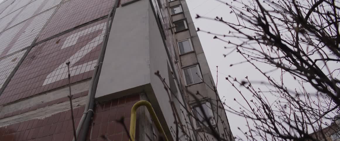 Tall residential building with tiled facade seen from below beside leafless branches