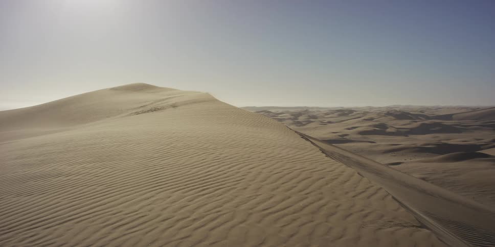 This video features a wide aerial view of a vast desert landscape filled with rolling sand dunes the scene captures the intricate rippled patterns on the sands surface under a clear bright sky