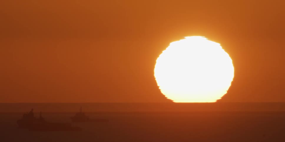 Large sun sets on the horizon while turning watercraft into silhouettes