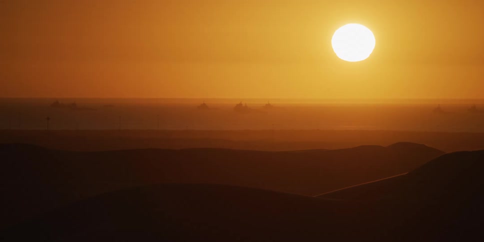 Low sun illuminates dunes and orange desert horizon