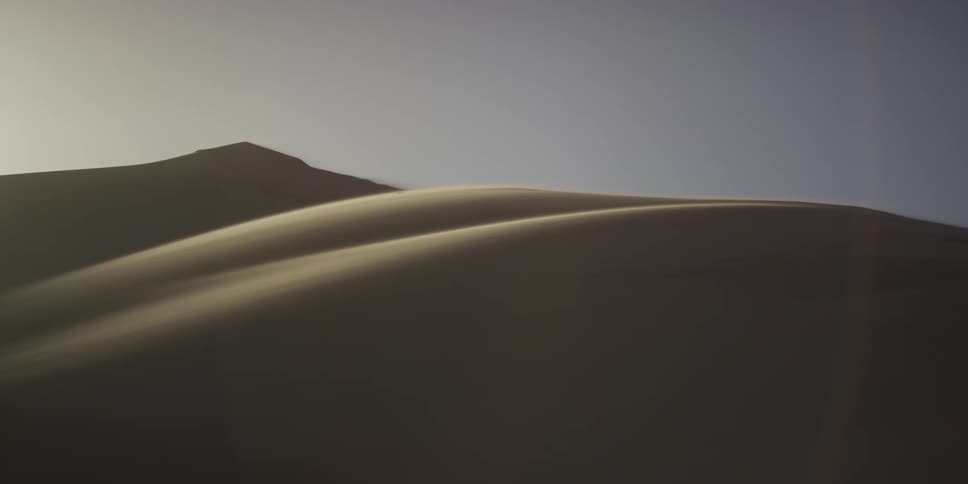 Sunlight shines on the desert sand dunes under a hazy sky