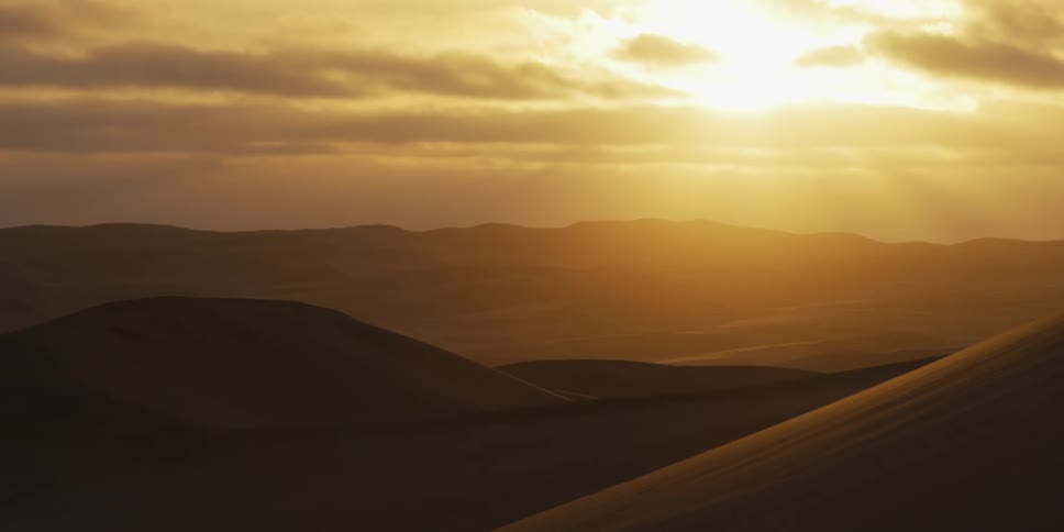 Golden sunlight breaks through heavy clouds over the vast sand dunes of the sahara desert as the bright light illuminates the rolling landscape during a warm sunset