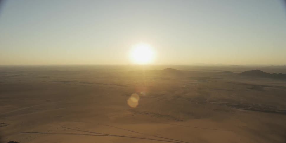 Sun shines from near the horizon across the desert and the mountains