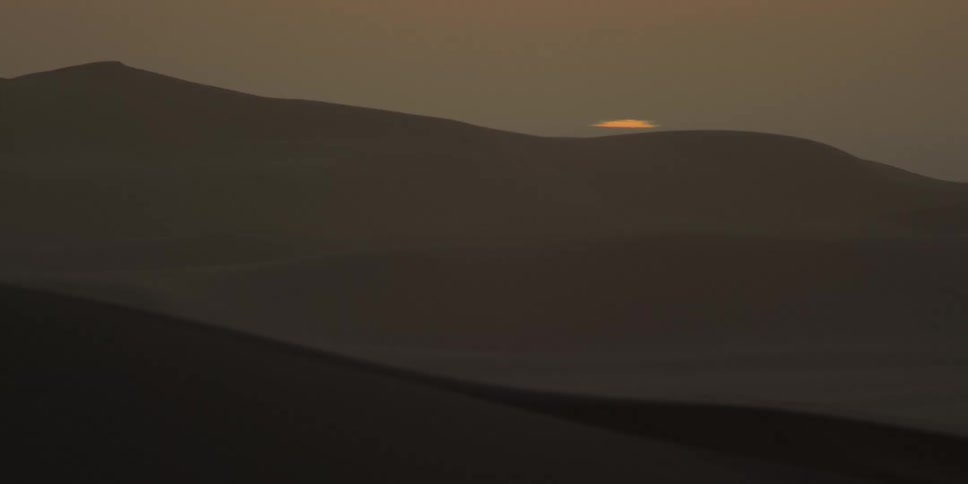 The sun sets behind mountains in a hazy sky