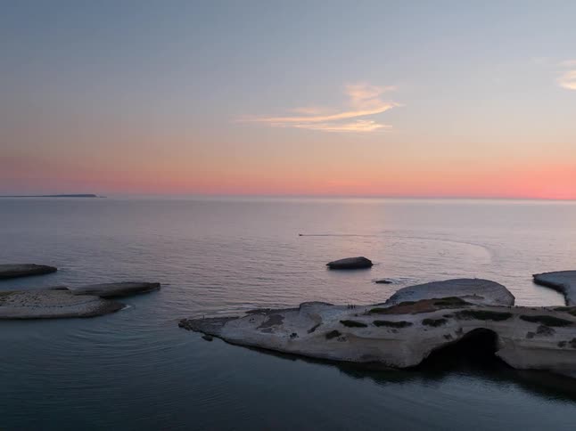Aerial view of rocky islets in calm sea under sunset sky
