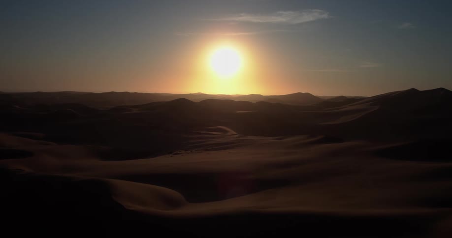 A group of people stands silhouetted against a bright rising sun on the crest of a vast sand dune the camera pulls back to reveal an expansive desert landscape stretching toward the horizon under a clear morning sky
