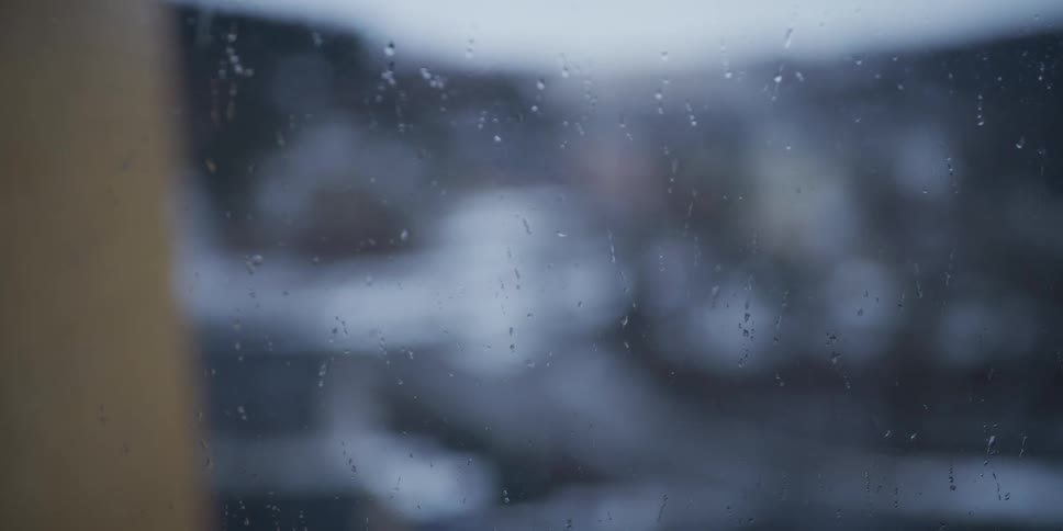 Raindrops running down glass with blurred urban background