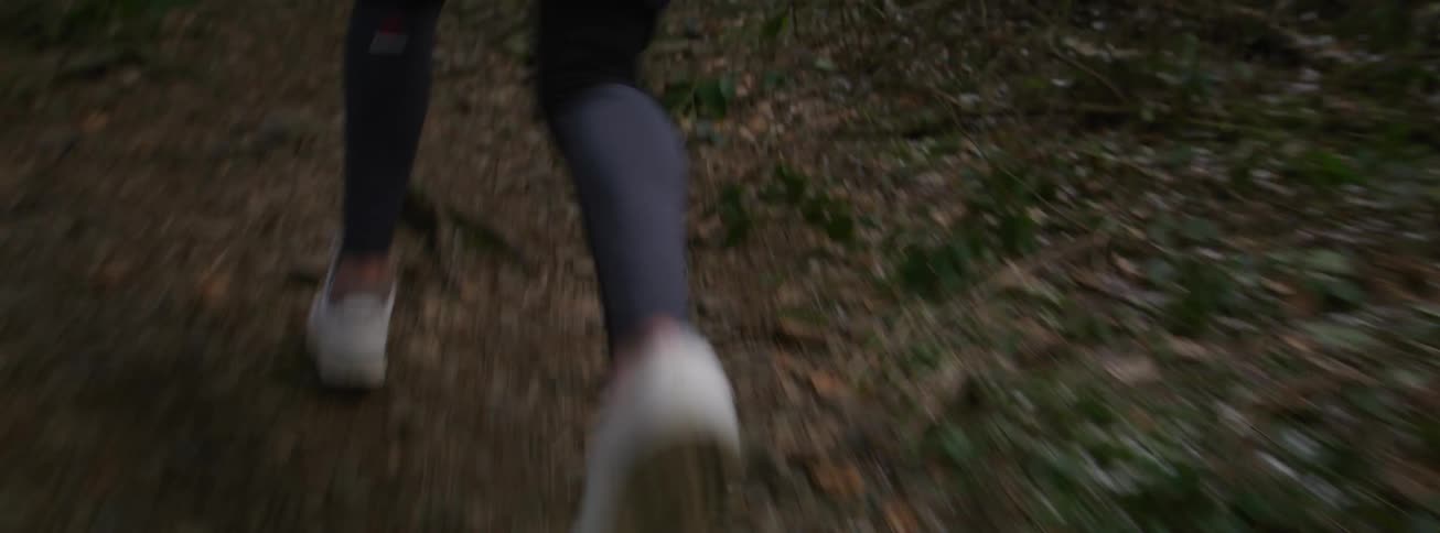 Feet in sneakers running along a dirt trail in a forest