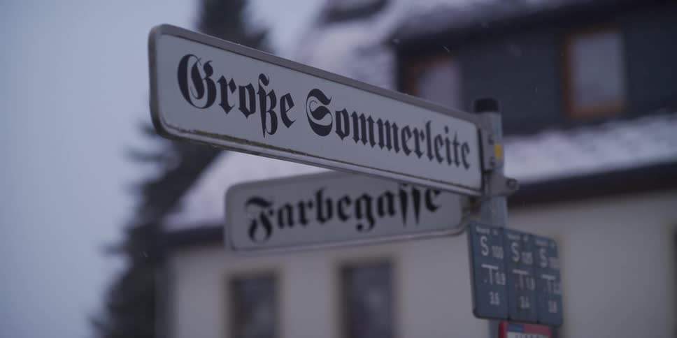 Street sign in front of a neighborhood house as snow falls