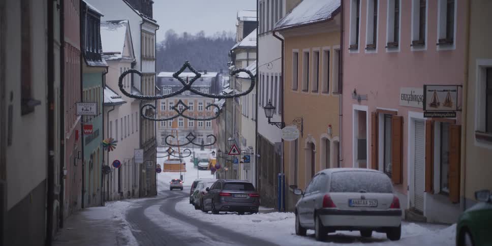 Narrow street with parked cars and snow between buildings
