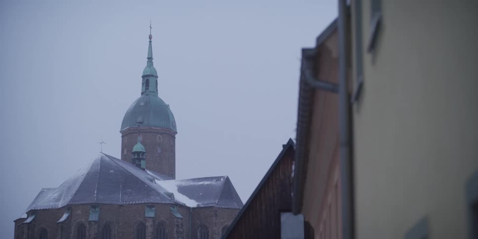 The ornate green dome and spires of saint annen church in annaberg buchholz rise above snow covered rooftops against a cold and foggy winter sky