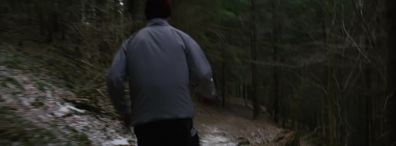 A person wearing a jacket running on a forest path in daylight with snow covering the ground