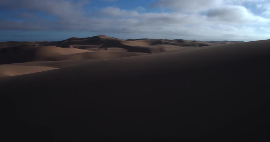 Dunes and mountains across the desert landscape under a cloudy sky