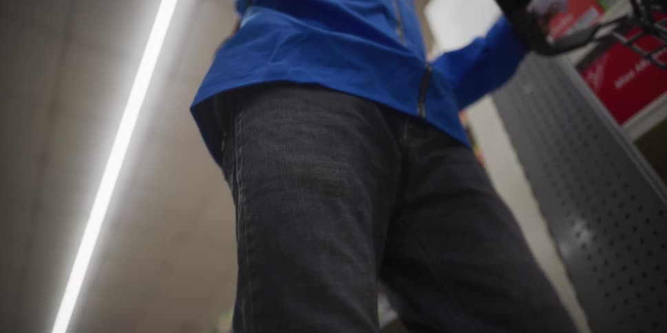 A person wearing a blue jacket and a face mask pushes a shopping cart through a grocery store aisle the lowangle shot focuses on the cart filled with canned goods and packaged items as it moves past stocked shelves