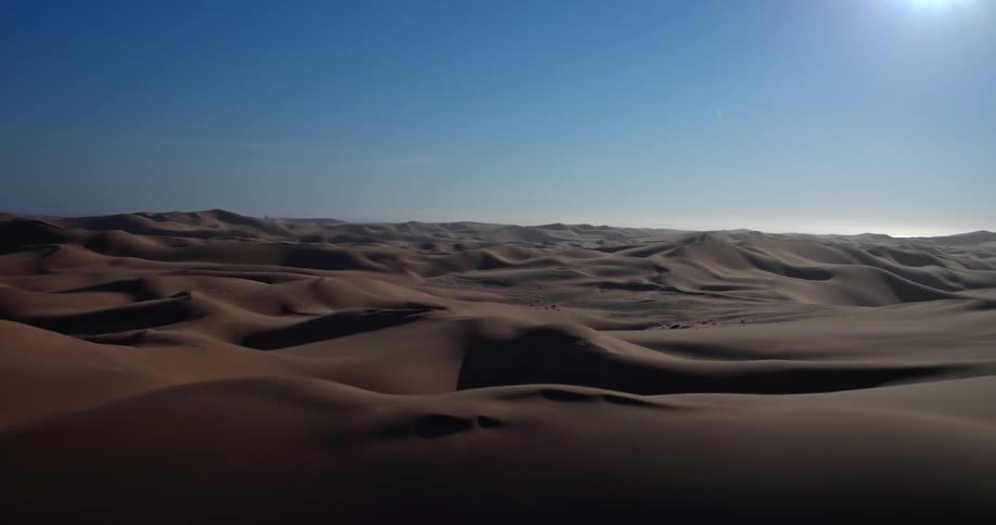 The sun shines brightly on dunes across the desert landscape