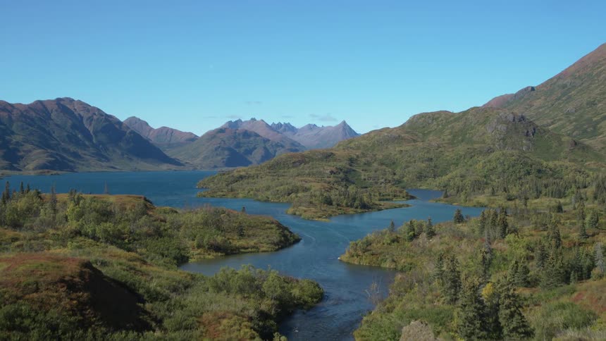 Boats sailing on the river in a forested mountain valley with mountains in the distance