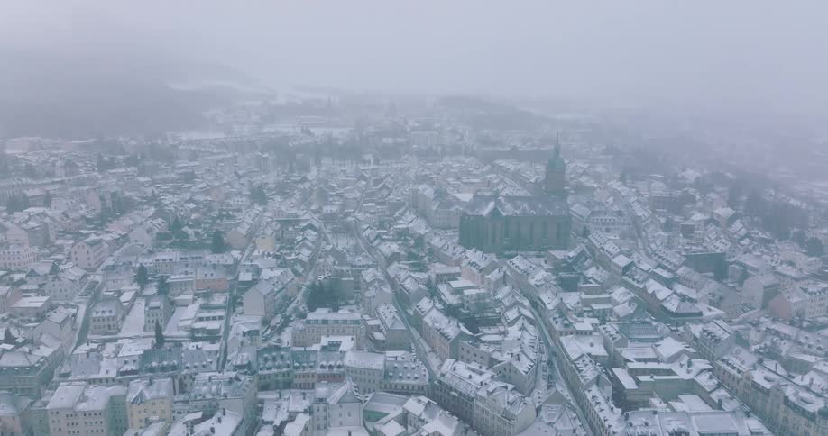 A city skyline at midday with a foggy atmosphere and rooftops covered in snow during winter