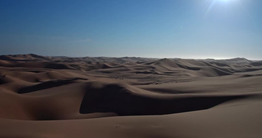 Dunes and mountains across the desert landscape as the sun shines brightly from above