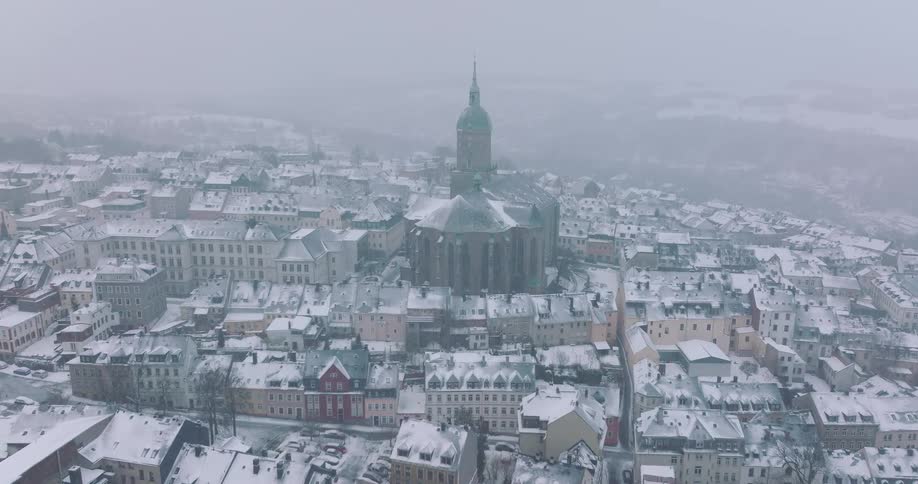 A city skyline view of a residential neighborhood with a cathedral in the midst of the city and rooftops covered in snow during winter at midday