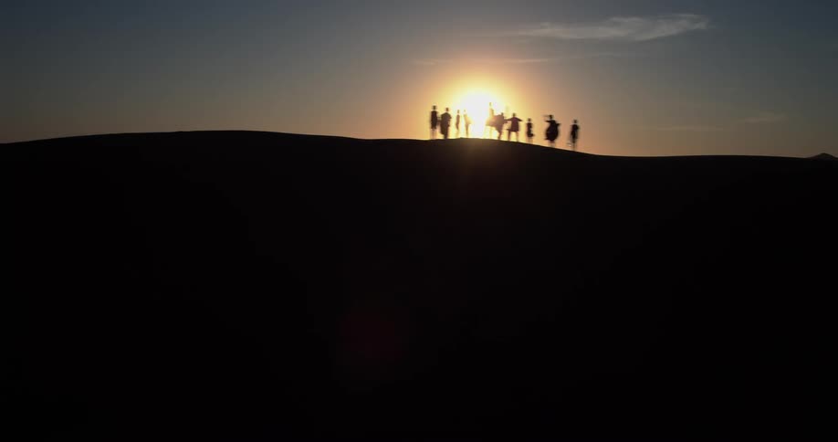 A sunny evening in the desert with a group of people standing and watching the setting sun