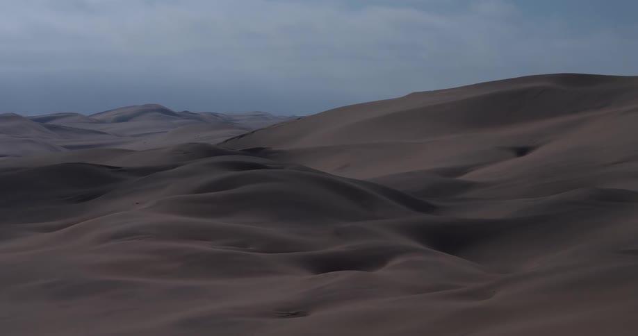 Dunes and mountains across the desert landscape under a cloudy sky