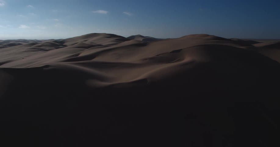 Rolling sand dunes stretch across the desert their smooth curves casting long shadows under the clear blue sky
