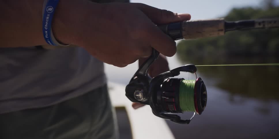 A man loosening a fishing line while standing on the bank of a river at midday