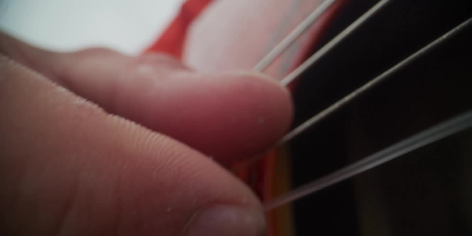 A person holding a red guitar outdoors striking the strings