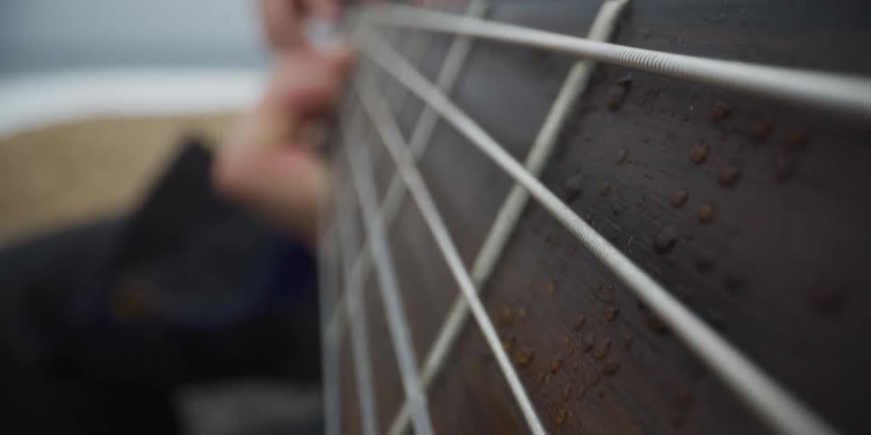 A person playing the strings of a guitar with their bare hands outdoors at midday