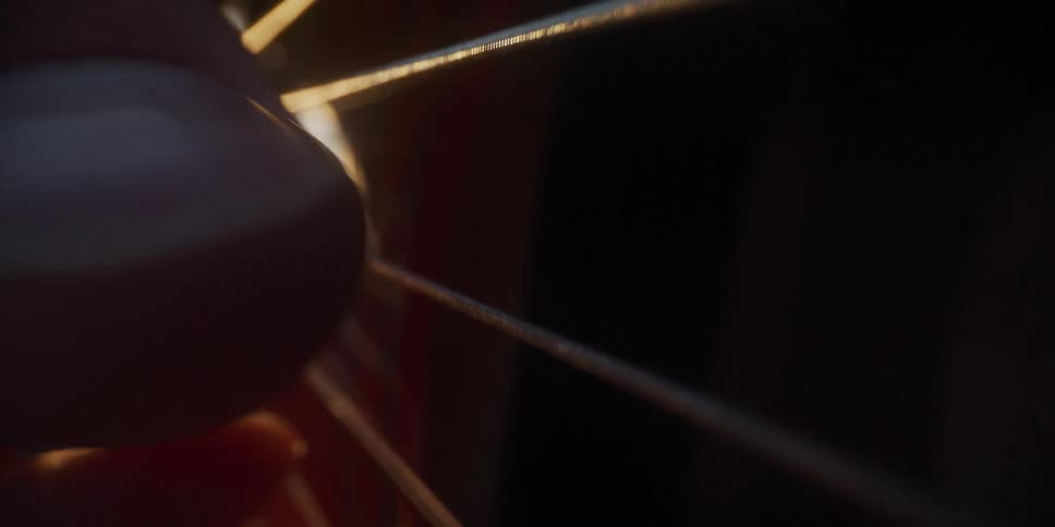 A close view shows fingers plucking the strings of an acoustic guitar as warm sunlight glows through the sound hole and highlights the intricate patterns of the rosette