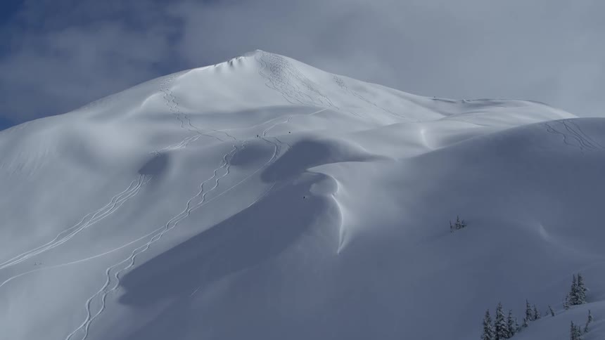 The video displays a snowcovered mountain peak with several visible tracks etched into the surface focusing on two prominent sets of lineson the left side of the frame there is a set of long winding tracks that curve gracefully down the