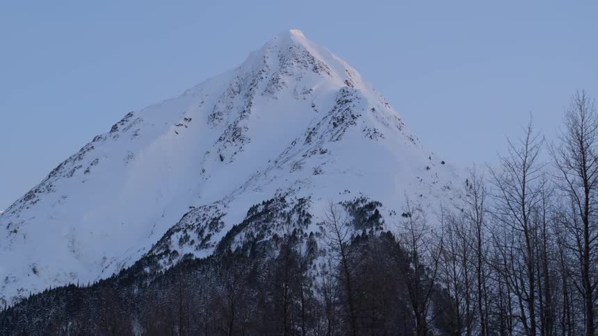 A tall mountain with a pointed peak is completely covered in snow