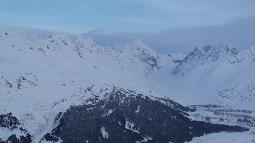 Forest covers the shorter mountains near the snow covered taller mountain in winter
