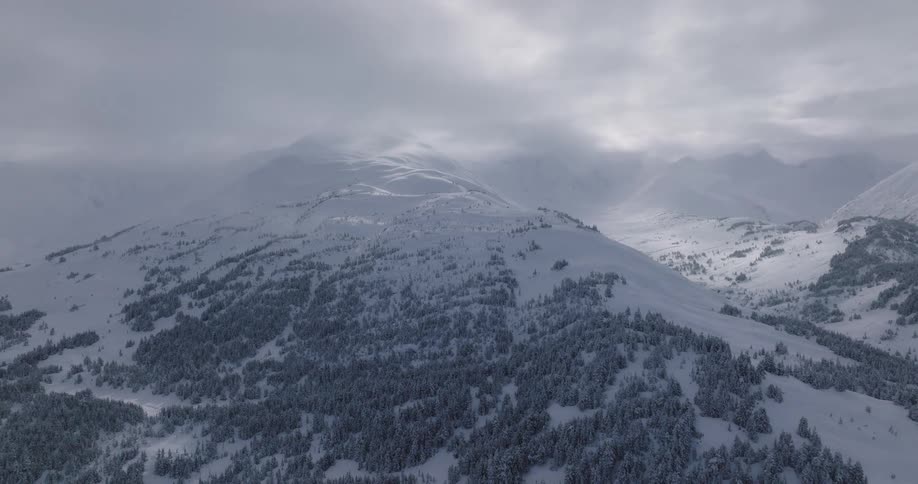A sprawling mountain range is covered with snow and the sky is cloudy